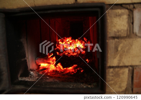 Smoldering burning coals in an open traditional brick oven. Black soot on the walls of the oven. Heat from the burning fire. Smoldering burning coals in an open traditional brick oven. Black soot on the walls of the oven. Heat from the burning fire. 120990645