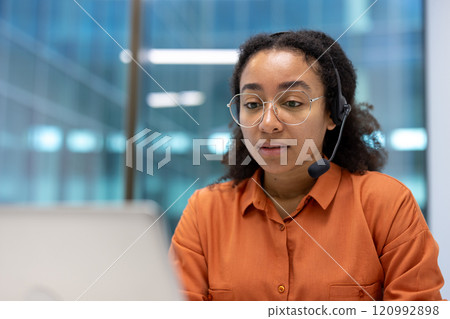A professional woman wearing a headset, engaging in a call at her computer. The office setting emphasizes communication and customer service. Her focused expression highlights dedication A professional woman wearing a headset, engaging in a call at her computer. The office setting emphasizes communication and customer service. Her focused expression highlights dedication 120992898