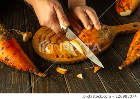 Bright orange beetroot vegetables are arranged alongside a wooden board as hands chop slices with precision. The warm lighting highlights the textures of the produce, showcasing culinary creativity Bright orange beetroot vegetables are arranged alongside a wooden board as hands chop slices with precision. The warm lighting highlights the textures of the produce, showcasing culinary creativity 120993074