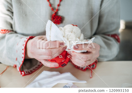 Crafting a white fabric doll with festive red accents. Highlighting folk art traditions and cultural heritage through handmade creations. 120993150