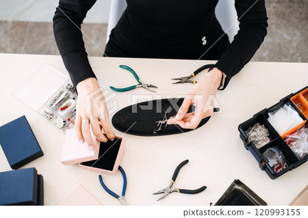 Artisan assembling handmade earrings in a sustainable workspace. Highlighting eco-conscious jewelry design and ethical craftsmanship. Artisan assembling handmade earrings in a sustainable workspace. Highlighting eco-conscious jewelry design and ethical craftsmanship. 120993155