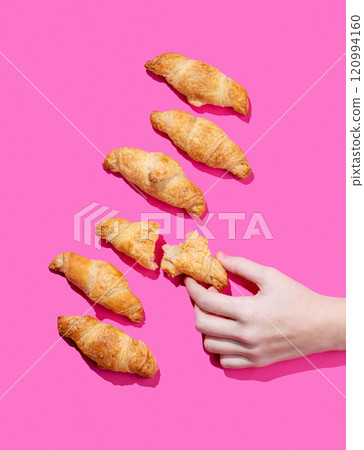 Hand holding fresh torn mini croissant on pink background with shadow. Design flat lay concept 120994160