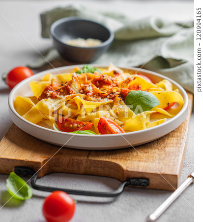 Homamade tagliatelle pasta with tomato sauce, basil and parmesan cheese in a plate on a wooden board 120994165