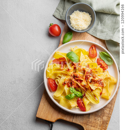 Tagliatelle pasta with tomato sauce, basil and parmesan cheese in a plate on a wooden board  120994166