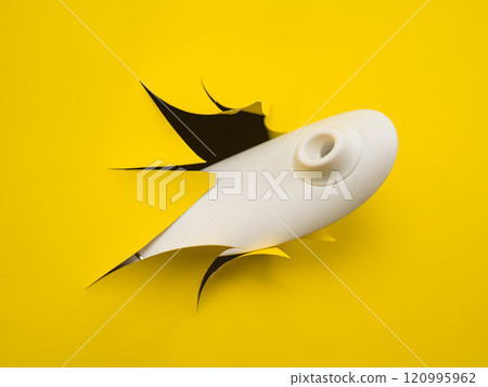Female hand holding white clitoral vacuum vibrator sticking out of yellow paper background.  120995962