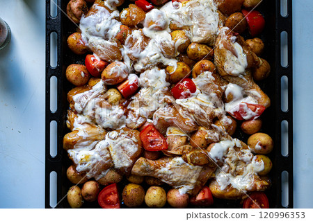 Baked chicken leg quarters seasoned with garlic and herbs with potatoes in a baking dish on a wooden table close up view 120996353