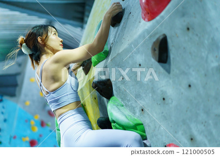 Healthy and sportive Asian woman is practicing a body strength sport training, woman climb an indoor rock climbing, Asian sport woman climb the artificial rock wall in the indoor gym. 121000505