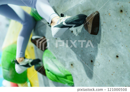 Healthy and sportive Asian woman is practicing a body strength sport training, woman climb an indoor rock climbing, Asian sport woman climb the artificial rock wall in the indoor gym. 121000508