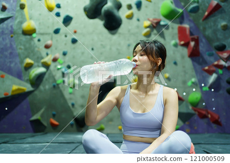 Asian beautiful woman is sitting on the floor and drinking water from bottle after finished practice in door rock climbing.  121000509