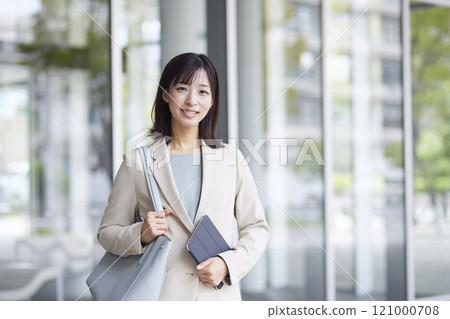一位面帶微笑的女上班族手持智慧型手機和文件站在那裡。 一位面帶微笑的女上班族手持智慧型手機和文件站在那裡。 121000708