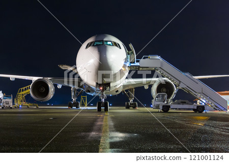 Front view of white wide-body passenger airplane with a boarding steps at the night airport apron 121001124