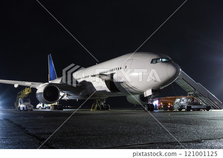 Wide-body passenger aircraft with air-stairs at the night airport apron. Airplane ground handling 121001125