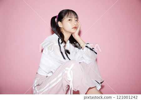 Cute portrait of a young woman in sporty clothes photographed against a pink background 121001242
