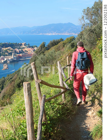 Man in sport clothes with backpack walk along path on mountain along sea and town. Hiking in mountain. Sport and health.  121002198