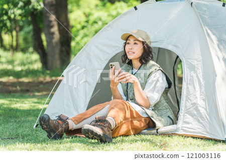 一位女士在露營地使用智慧型手機享受露營和豪華露營的樂趣 121003116