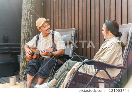 A couple relaxing while playing the ukulele and sitting in a reclining chair 121003744