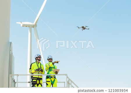 Team of electrical engineer is perform the inspection and maintenance of electric generating windmill turbine. Team of professional electrical engineers in fully safety suit are working and discussing 121003934