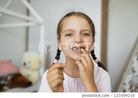 Little Caucasian girl smiling and holding first lost baby tooth in cozy home environment showcasing childhood milestone. Little Caucasian girl smiling and holding first lost baby tooth in cozy home environment showcasing childhood milestone. 121004210