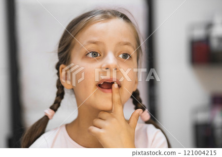 Little Caucasian girl with fallen milk teeth touches loose tooth while looking in mirror in bathroom. Moment captures curiosity and childhood growth. 121004215