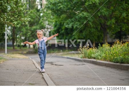 The girl walks along the curb, balancing with her arms outstretched The girl walks along the curb, balancing with her arms outstretched 121004356
