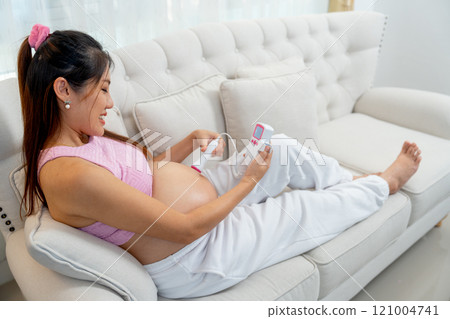Back of Asian pregnant woman lie on sofa and use tools for listen sound in her belly and look happy at home. 121004741