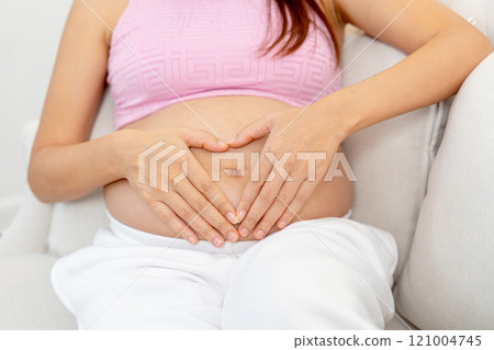 Close up pregnant woman sit on sofa and put hands on her belly with heart shape. Close up pregnant woman sit on sofa and put hands on her belly with heart shape. 121004745