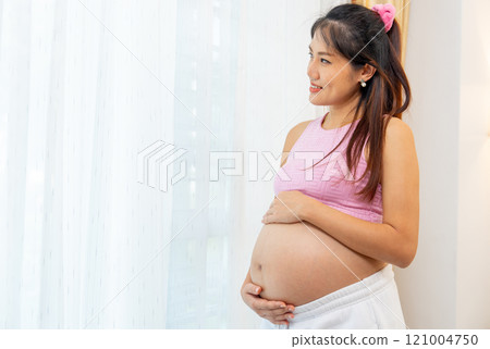 Asian pregnant woman stand with smiling in front of white curtain also look outside with happiness. Asian pregnant woman stand with smiling in front of white curtain also look outside with happiness. 121004750
