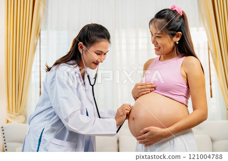 Asian woman doctor use stethoscope to check health of the baby in the belly of pregnant woman during healthcare for mother at home. 121004788