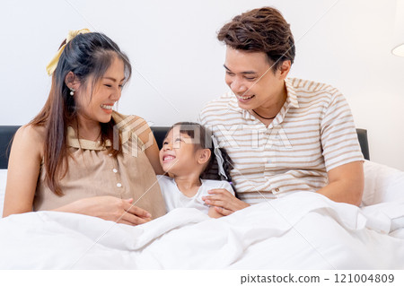 Close up Asian family with pregnant mother, father and little daughter enjoy to stay on bed together in bedroom of their house. 121004809