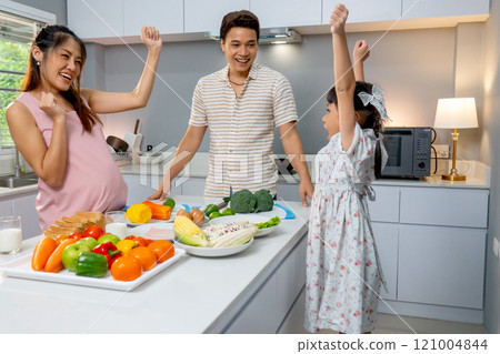 Asian family with pregnant mother, father and little girl express action of happiness in the kitchen of their house. 121004844
