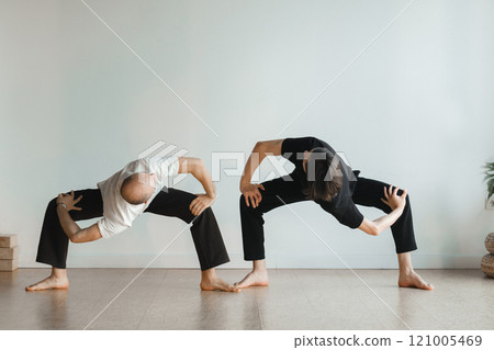 two young athletes practice yoga in the gym. Joint training, indoors, studio. The concept of a healthy lifestyle two young athletes practice yoga in the gym. Joint training, indoors, studio. The concept of a healthy lifestyle 121005469