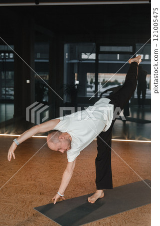 An athletic young man does exercises in the fitness room. A professional guy does yoga in the gym 121005475