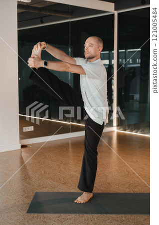 An athletic young man does exercises in the fitness room. A professional guy does yoga in the gym An athletic young man does exercises in the fitness room. A professional guy does yoga in the gym 121005484