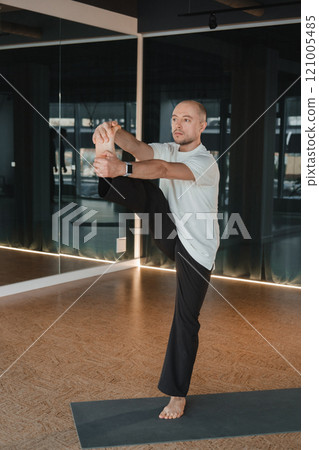 An athletic young man does exercises in the fitness room. A professional guy does yoga in the gym 121005485