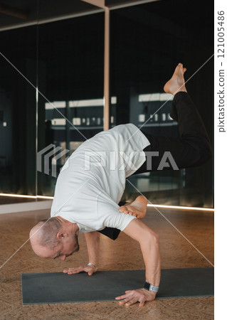 An athletic young man does exercises in the fitness room. A professional guy does yoga in the gym An athletic young man does exercises in the fitness room. A professional guy does yoga in the gym 121005486