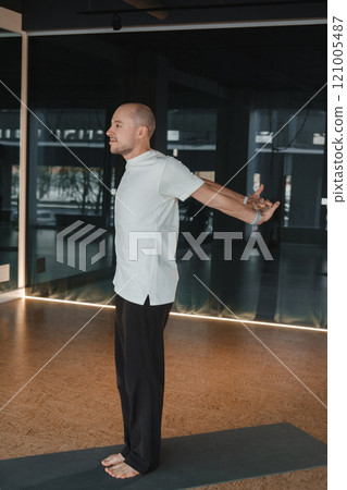 An athletic young man does exercises in the fitness room. A professional guy does yoga in the gym 121005487