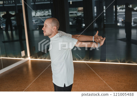 An athletic young man does exercises in the fitness room. A professional guy does yoga in the gym An athletic young man does exercises in the fitness room. A professional guy does yoga in the gym 121005488