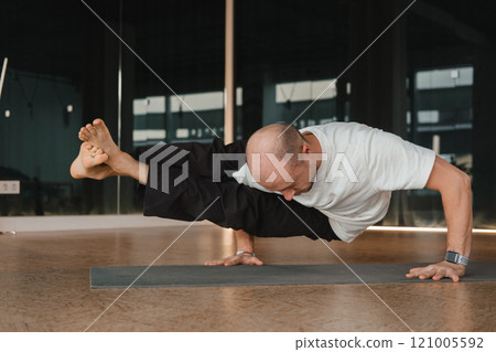 An athletic young man does exercises in the fitness room. A professional guy does yoga in the gym 121005592