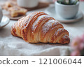 Golden brown croissant with flaky layers, dusted with powdered sugar, perfect for breakfast or snack. Enjoy its buttery texture and delightful taste 121006044
