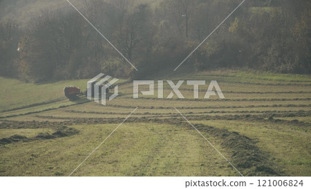 A tractor with hay baler or hay maker trailer in the green field A tractor with hay baler or hay maker trailer in the green field 121006824