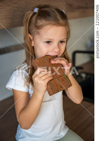 Little girl eating Dubai chocolate with pistachio paste and kataifi dough. Confectionery handmade sweets at home in the kitchen.  121007406