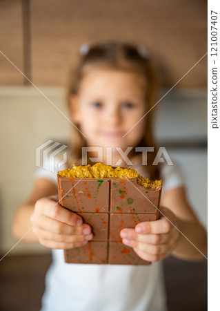 Dubai chocolate with pistachio paste and kataifi dough in hands of little girl. Confectionery handmade sweets at home in the kitchen. Dubai chocolate with pistachio paste and kataifi dough in hands of little girl. Confectionery handmade sweets at home in the kitchen. 121007407