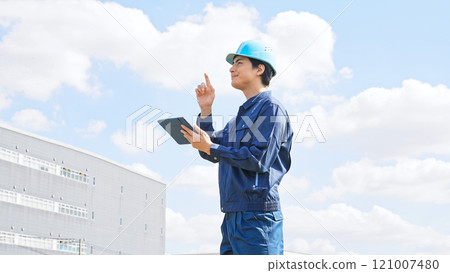 A male worker using a tablet PC in front of a factory-like building 121007480