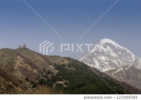 A breathtaking view of Mount Kazbek in Georgia, with its snow-capped peak rising majestically under a clear blue sky. A breathtaking view of Mount Kazbek in Georgia, with its snow-capped peak rising majestically under a clear blue sky. 121009385