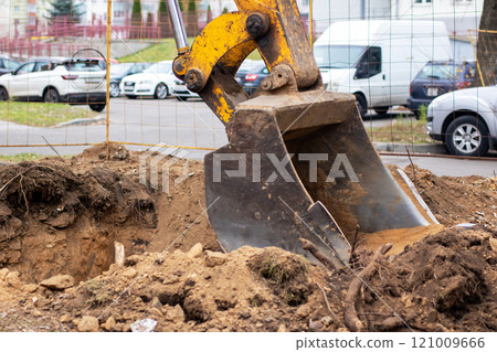 A bright yellow excavator is actively digging a hole in the ground A bright yellow excavator is actively digging a hole in the ground 121009666