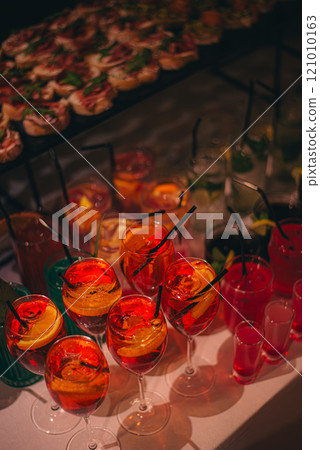 Chilled alcoholic cocktails served on the rocks with rosemary garnish displayed in rows on a buffet table in elegant glasses at a catered event 121010163