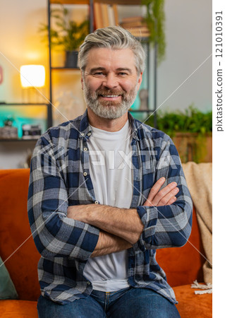 Happy smiling Caucasian senior middle-aged man sitting on sofa looking at camera and smiling at home 121010391