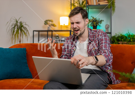 Upset man using laptop having anxiety and stress loss bad lottery game results news at home room Upset man using laptop having anxiety and stress loss bad lottery game results news at home room 121010398