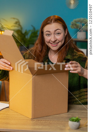 Happy woman shopper unpacking cardboard box delivery parcel online shopping purchase at home office Happy woman shopper unpacking cardboard box delivery parcel online shopping purchase at home office 121010497