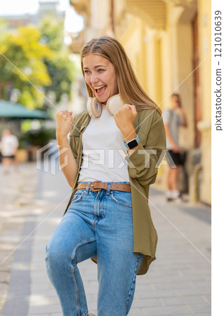 Excited happy woman traveler shouting, celebrating success, winning clenching fists on city street 121010639
